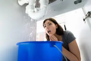 A woman using a bucket to collect water from a leaking pipe in an Irving, TX home.